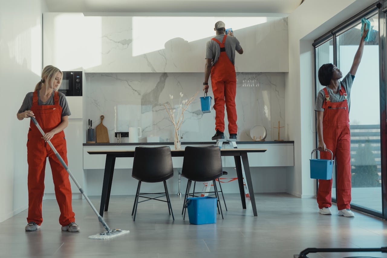 hero-img Group of cleaners in red uniforms mopping and wiping glass in a modern dining room.